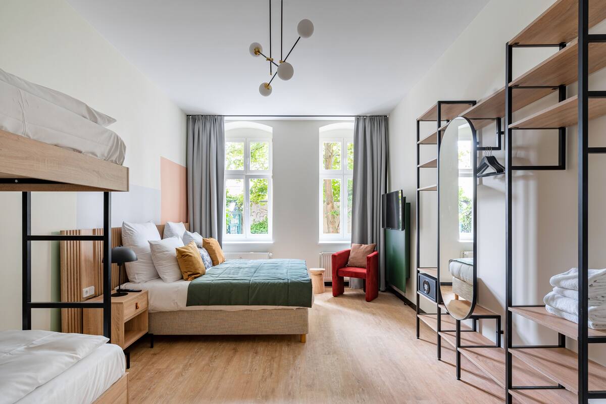 A modern bedroom with a bunk bed, a single bed, a desk, a chair, a TV, and a large window with curtains.