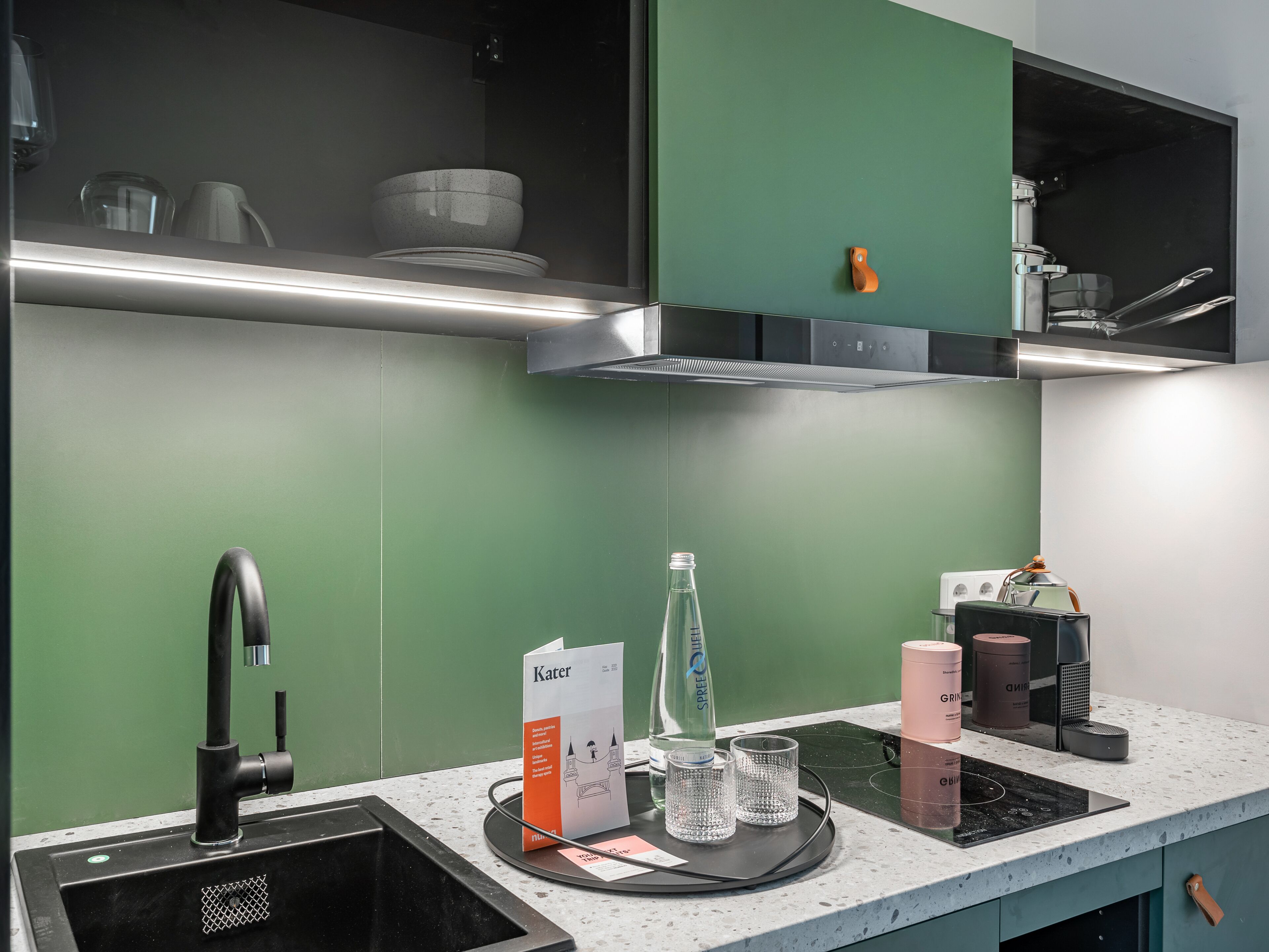 A modern kitchen with a black faucet, a stainless steel range hood, and a green backsplash.