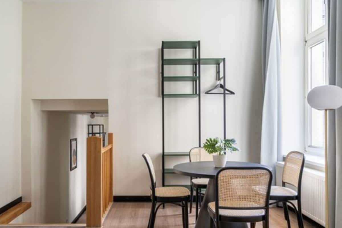 A modern dining area with a round table, four chairs, a potted plant, and a wall-mounted rack.