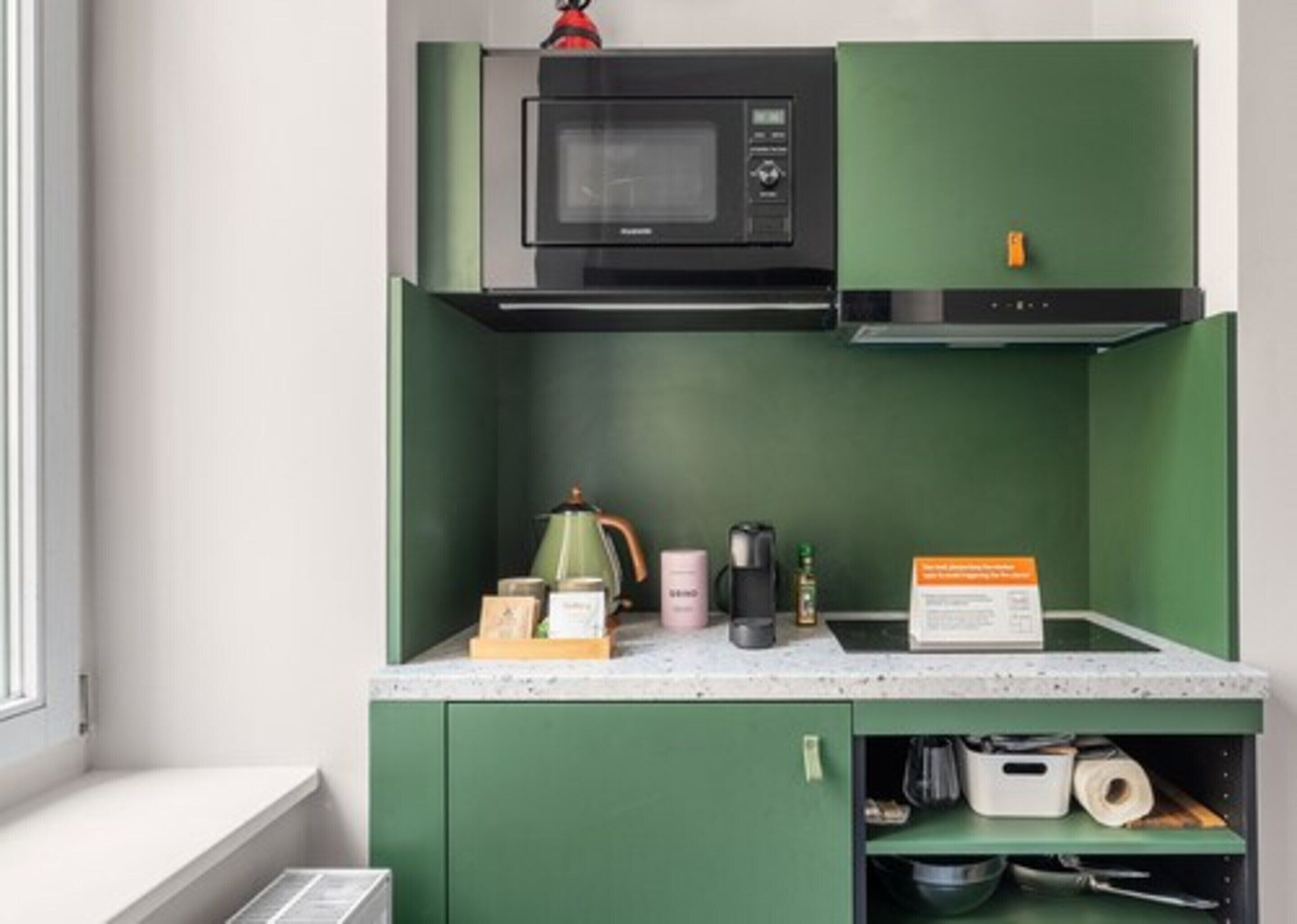 A compact kitchen with a microwave, kettle, and coffee maker on the countertop.