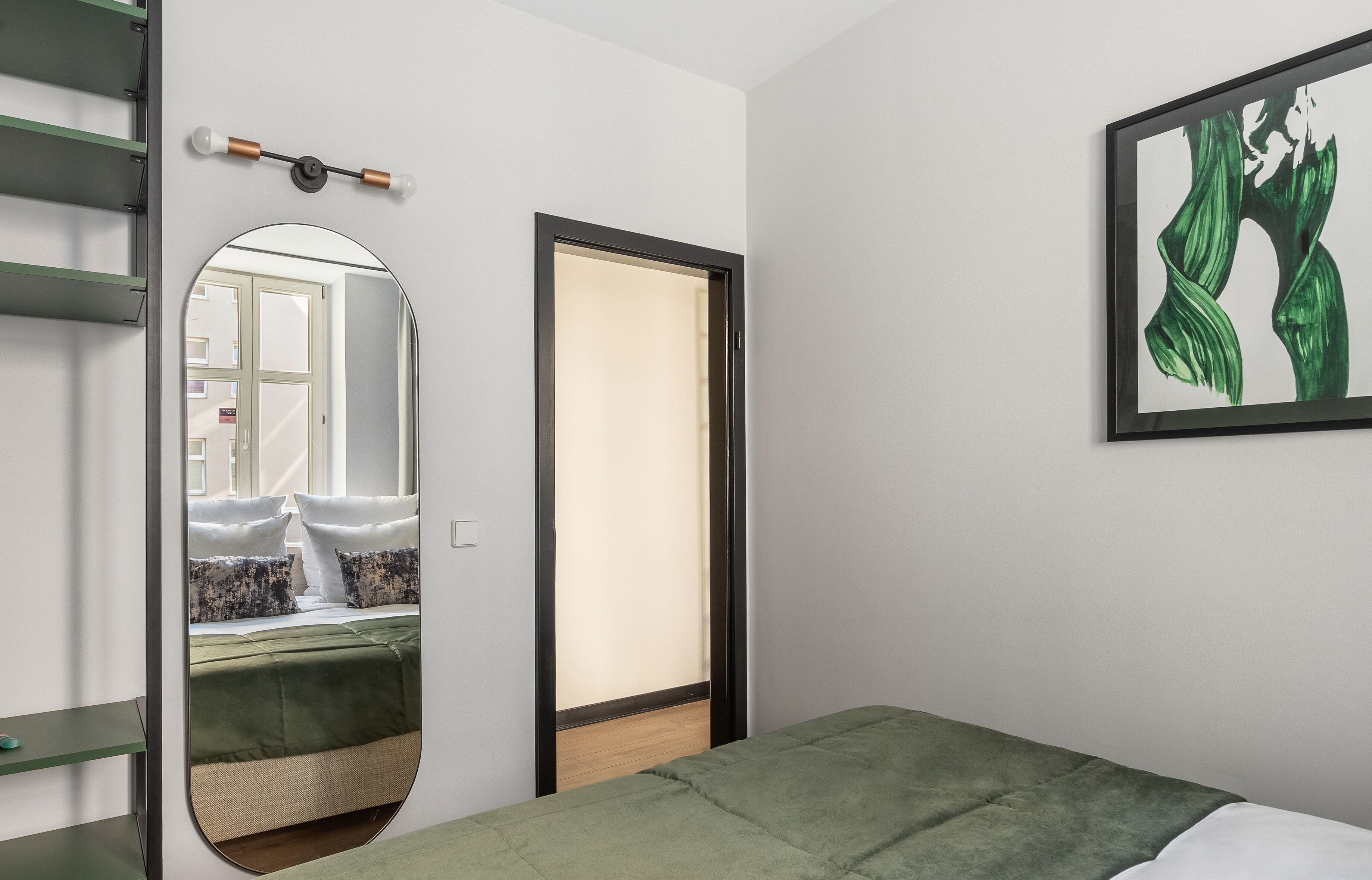 Ein Schlafzimmer mit einem Bett, einem Spiegel, einem gerahmten Kunstwerk und einer Tür zu einem anderen Raum.
