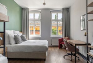A modern hotel room with a large bed, a desk, and a view of the city through large windows. - Numa Berlin Kater (Berlin)