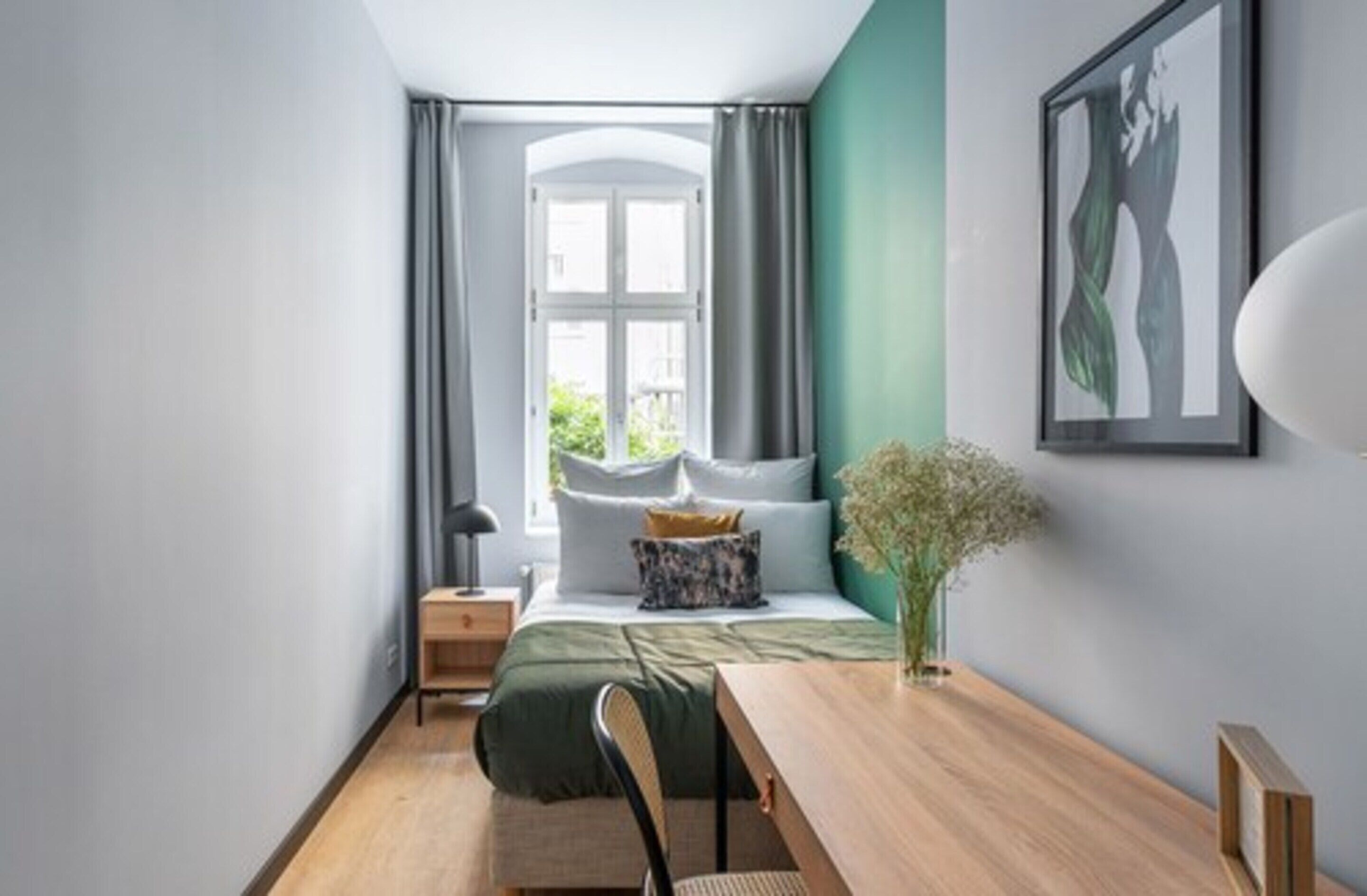 Ein modernes Schlafzimmer mit Bett, Nachttisch, Lampe und Blick ins Freie durch ein Fenster.