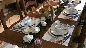 Een eettafel gedekt met witte borden, kopjes en bestek, versierd met witte rozen en een broodmand.