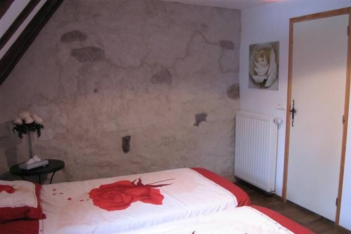 Een slaapkamer met een schuine kap, een radiator, een deur en een muur met een bloemstuk.
