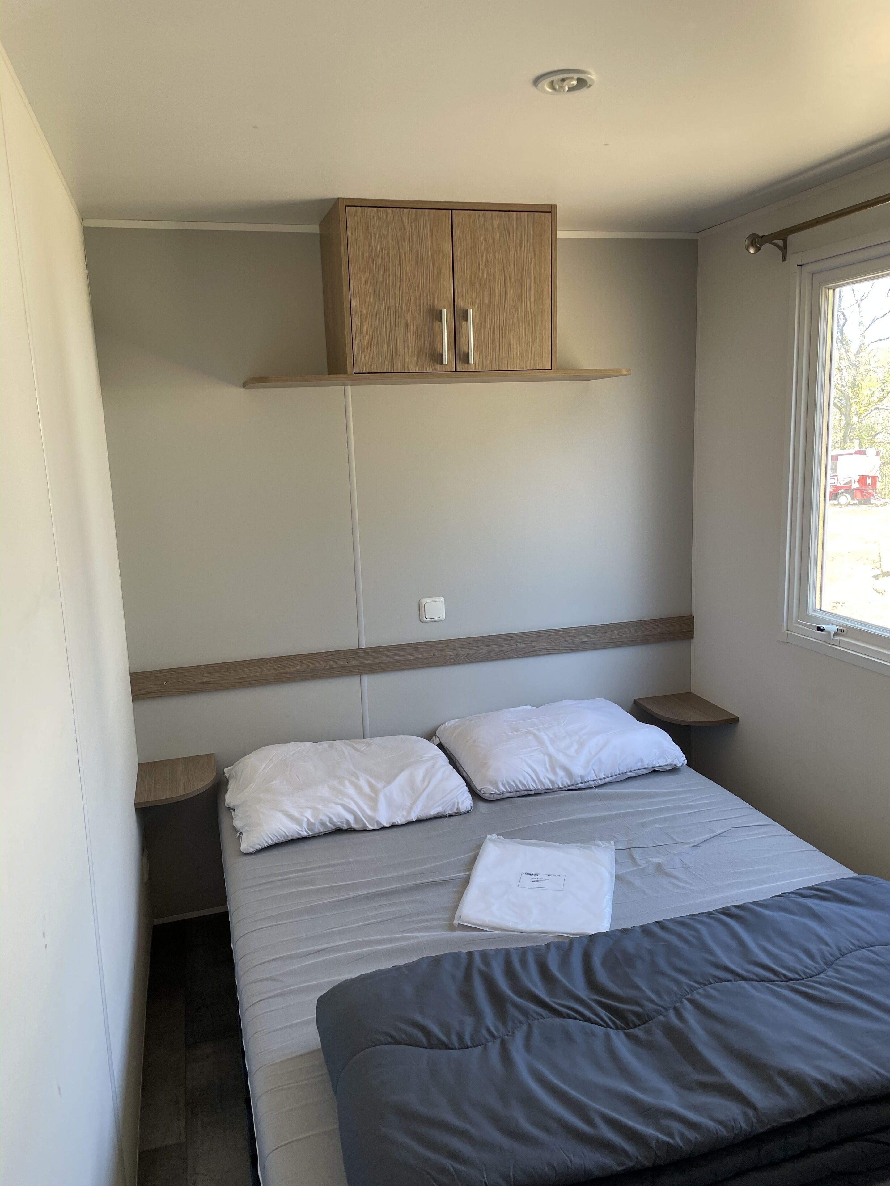 A bedroom with a bed, two bedside tables, a wooden wardrobe, and a window with a view.
