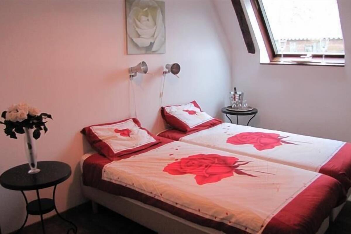 Een slaapkamer met twee bedden, een tafeltje, een vaas met bloemen en een raam met uitzicht.