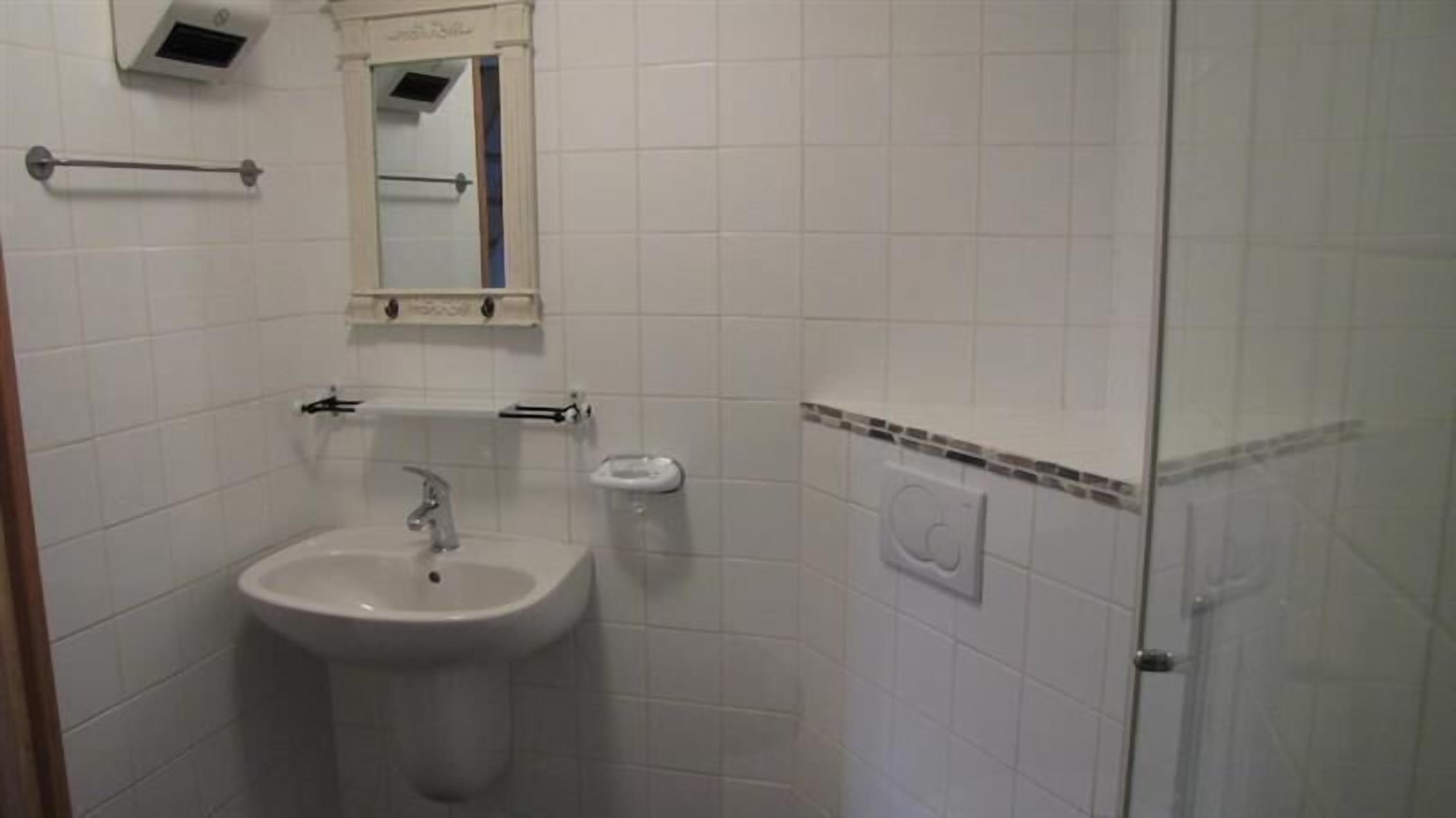 A bathroom with a sink, mirror, towel rack, and a shower area.