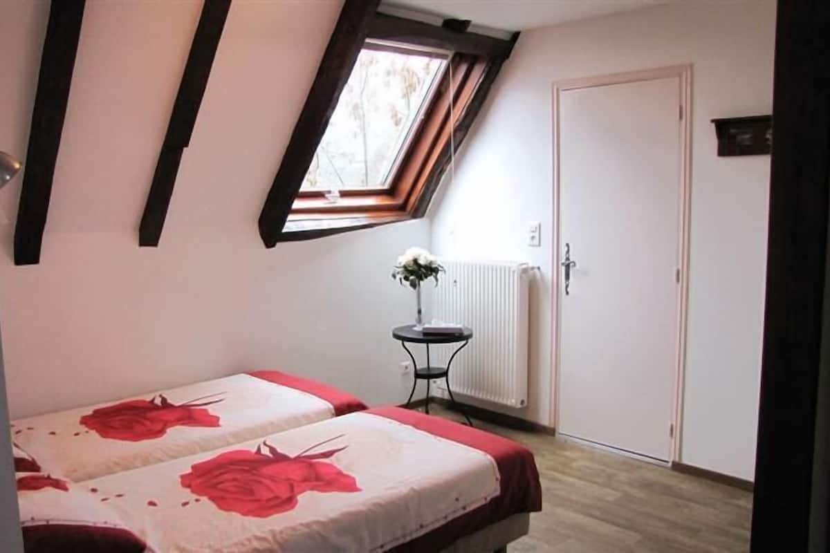 Een slaapkamer met twee bedden, een radiator, een kleine tafel met een vaas en een raam met uitzicht op bomen.