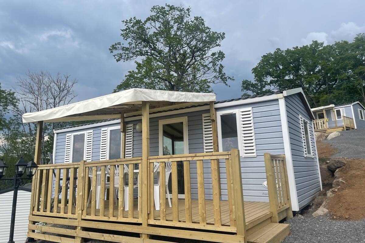 Een kleine, gelijkvloerse stacaravan met een houten terras en een overdekte veranda.