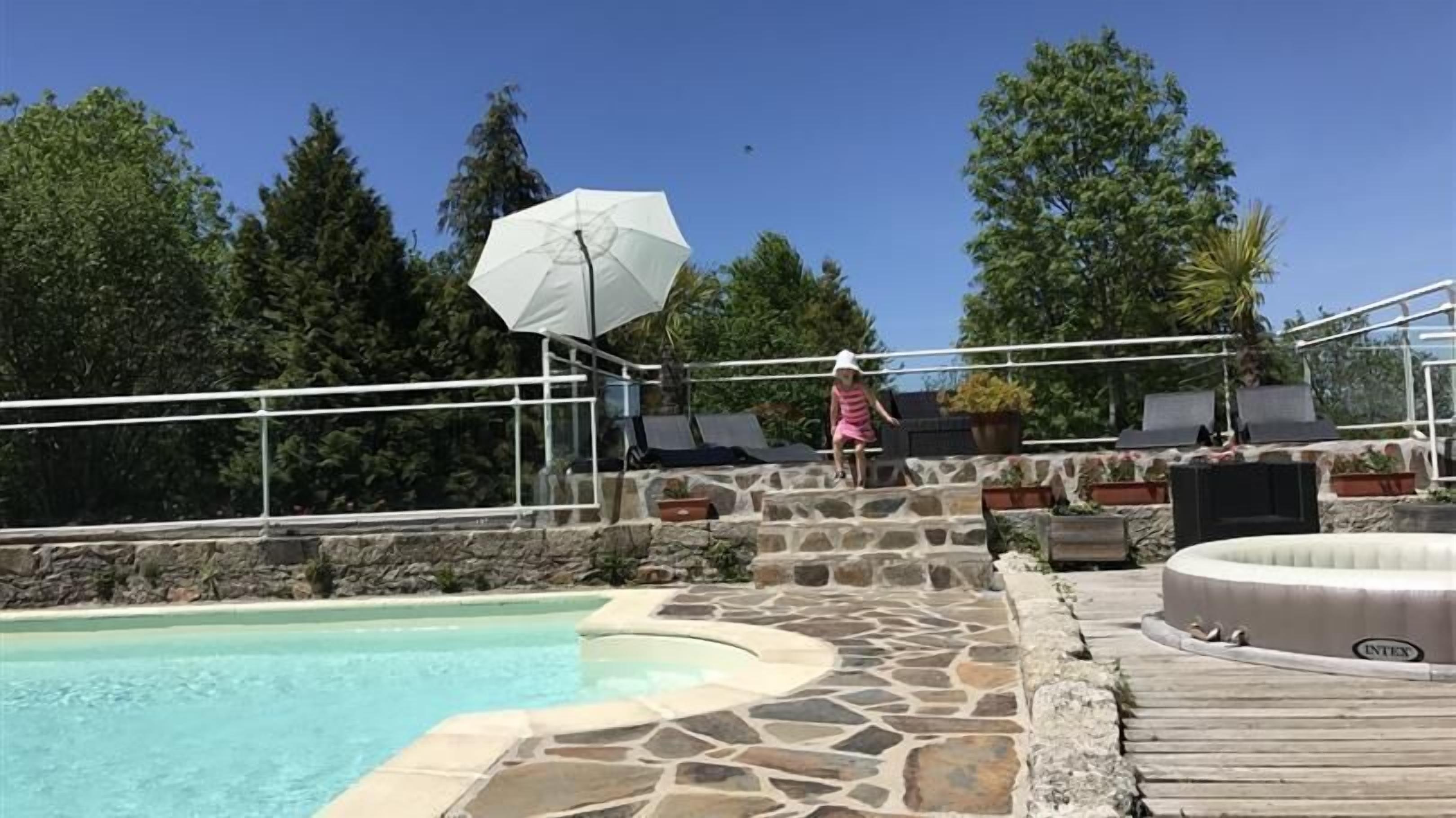 A pool area with stone steps, lounge chairs, and a hot tub.