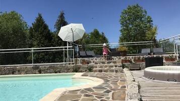 A pool area with stone steps, lounge chairs, and a hot tub.