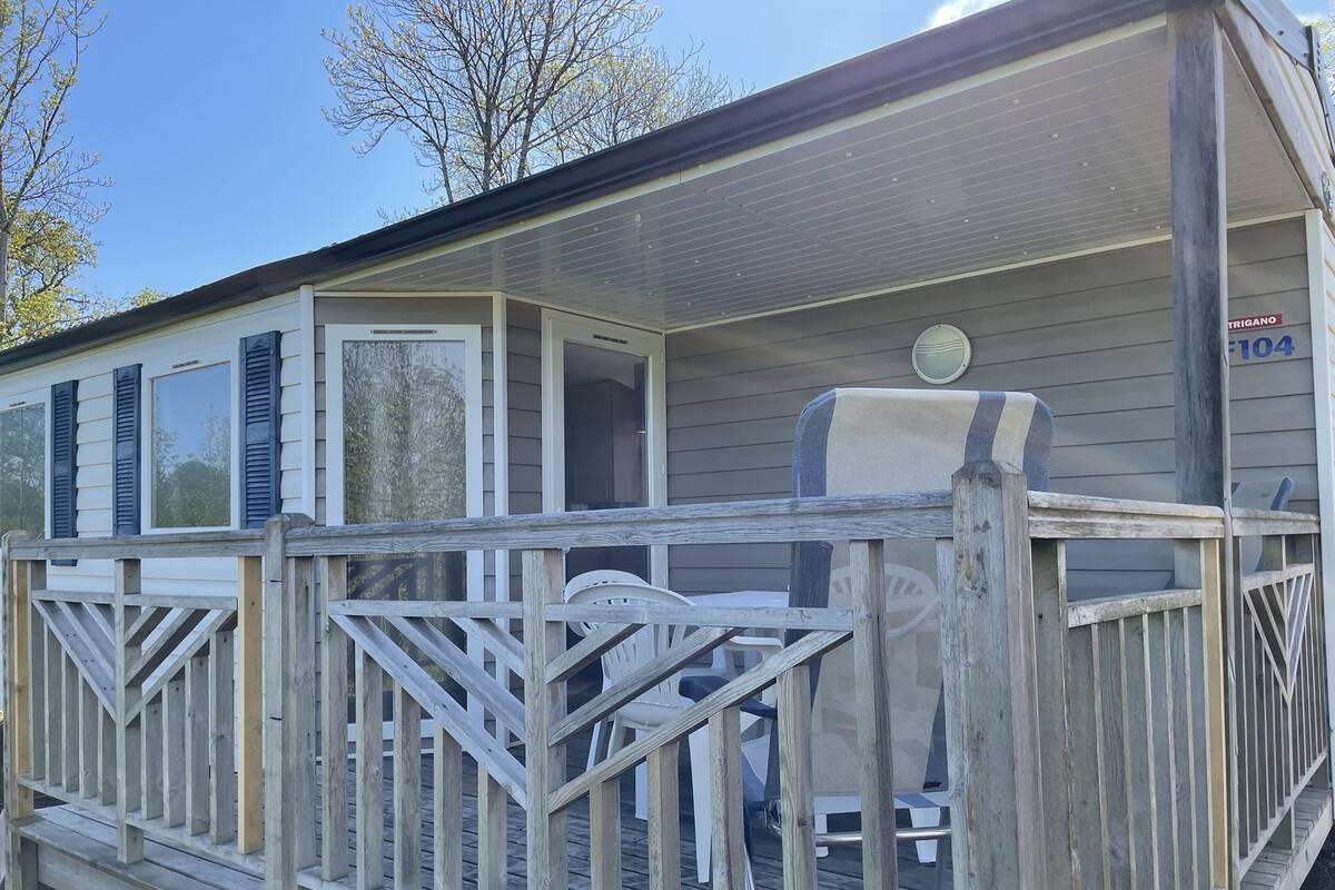 Een houten terras met een balustrade, een overdekte veranda en een stoel.