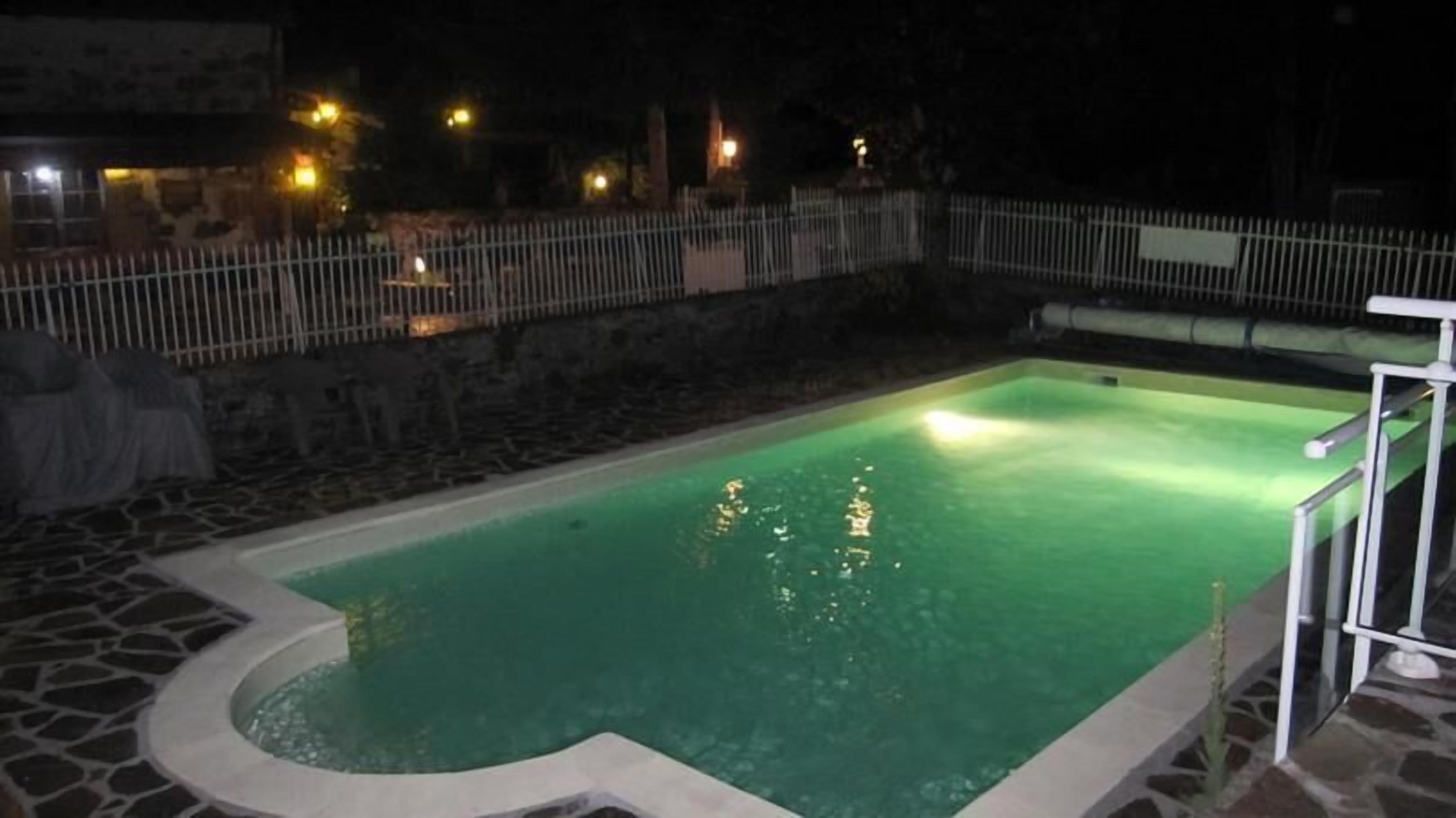 Une piscine bordée de pierres et entourée d’une clôture métallique.