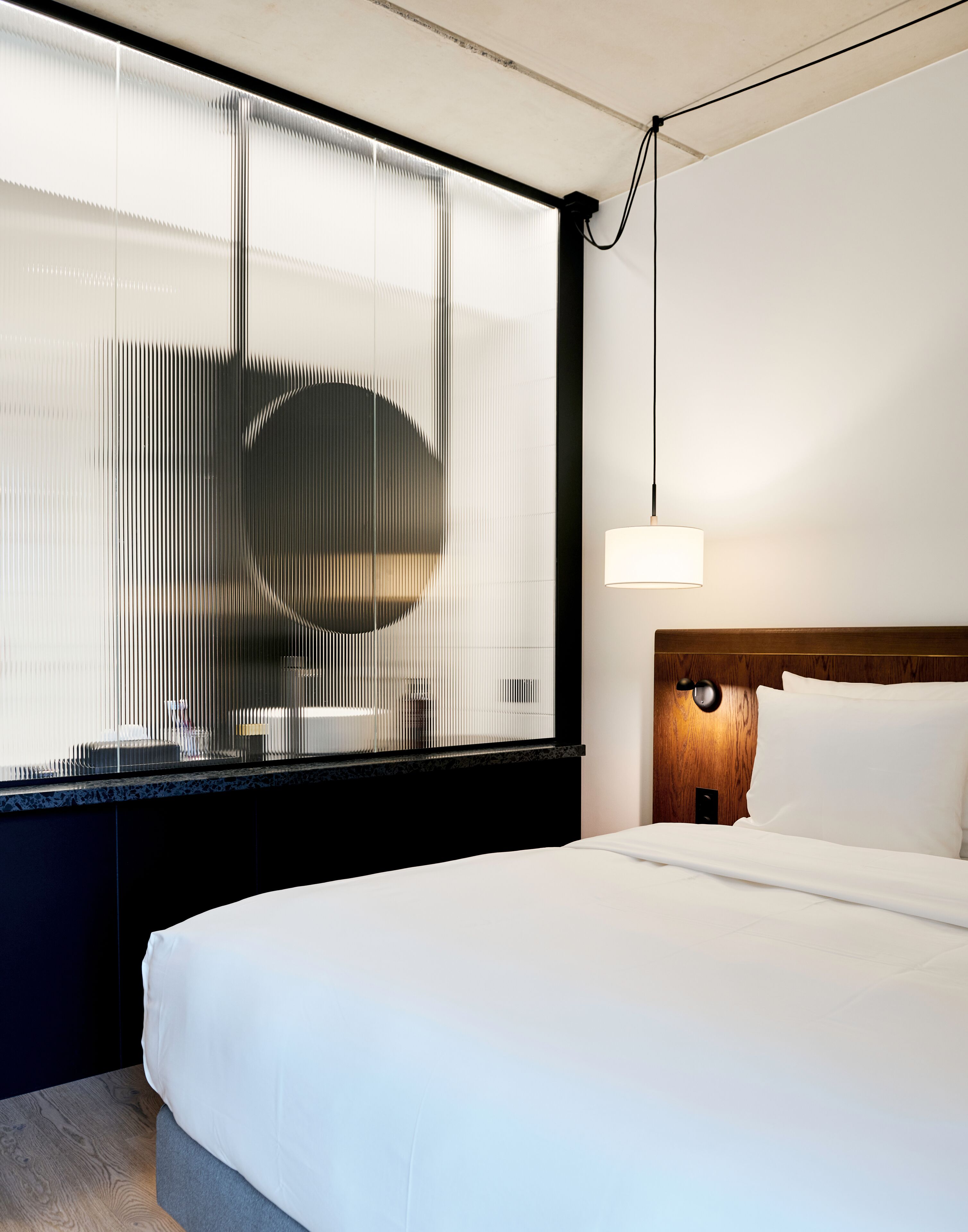 Ein Hotelzimmer mit einem großen Bett, einem hölzernen Kopfteil, einer Wandlampe und einem Fenster mit Jalousien.