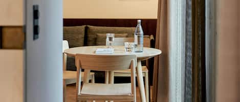Un comedor moderno con una mesa redonda, sillas de madera y un sofá. Hay una botella y copas sobre la mesa, y una obra de arte en la pared.