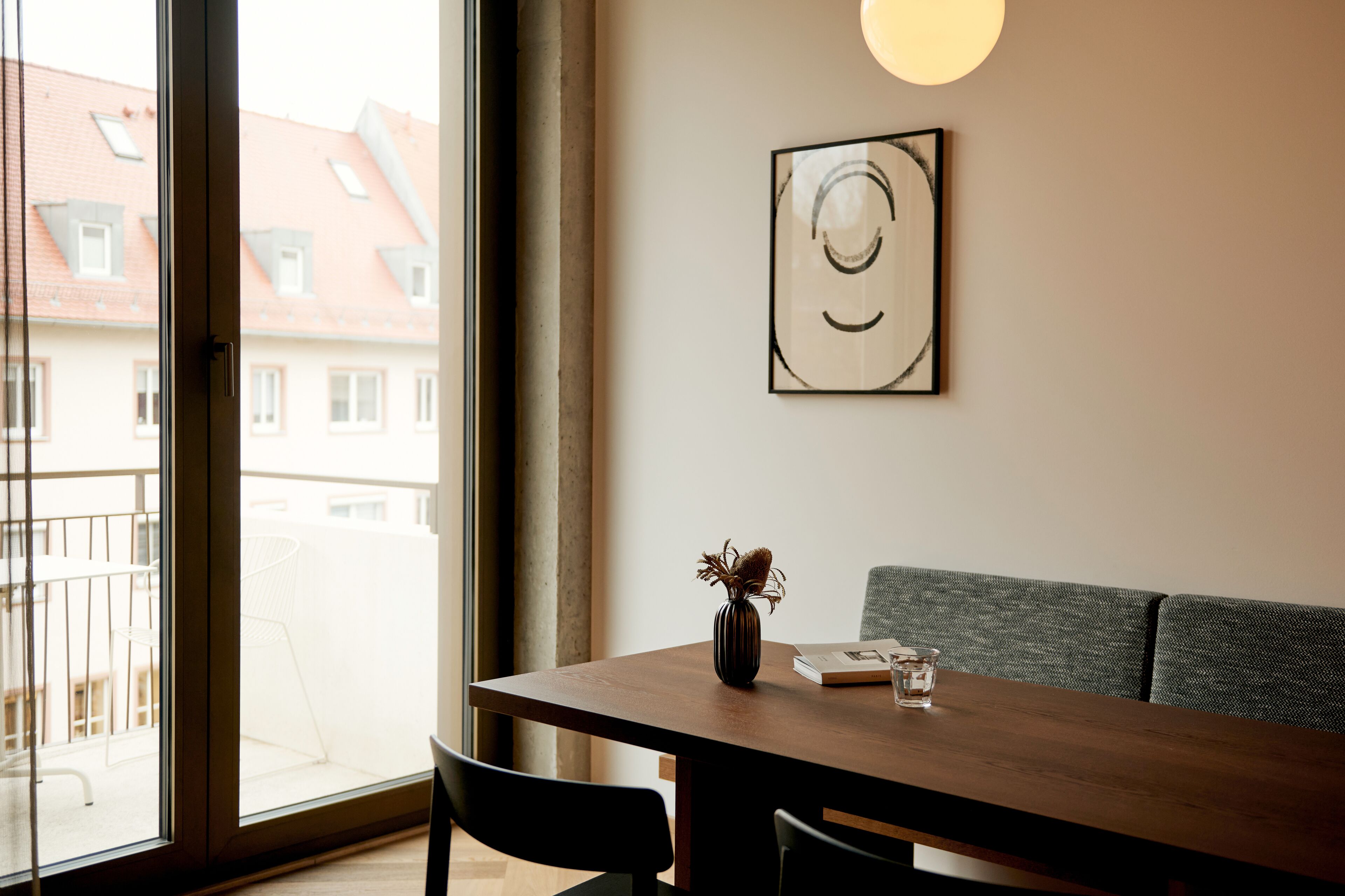 A modern dining area with a wooden table, a vase with dried flowers, and a framed artwork on the wall.