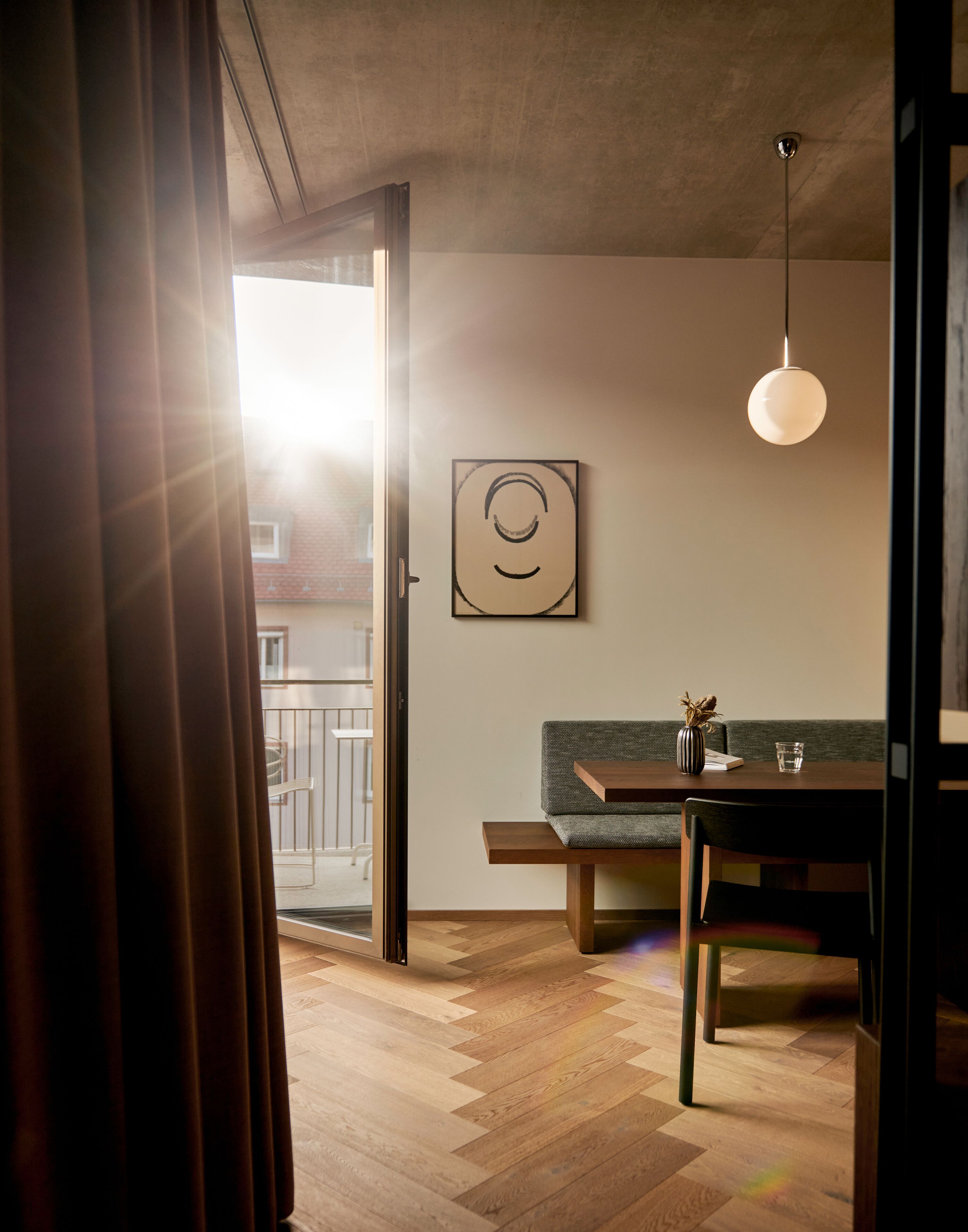 Un interior moderno con piso de madera en patrón de espiga, un sofá verde, una mesa de comedor de madera y una lámpara colgante.