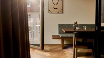 Un interior moderno con piso de madera en patrón de espiga, un sofá verde, una mesa de comedor de madera y una lámpara colgante.