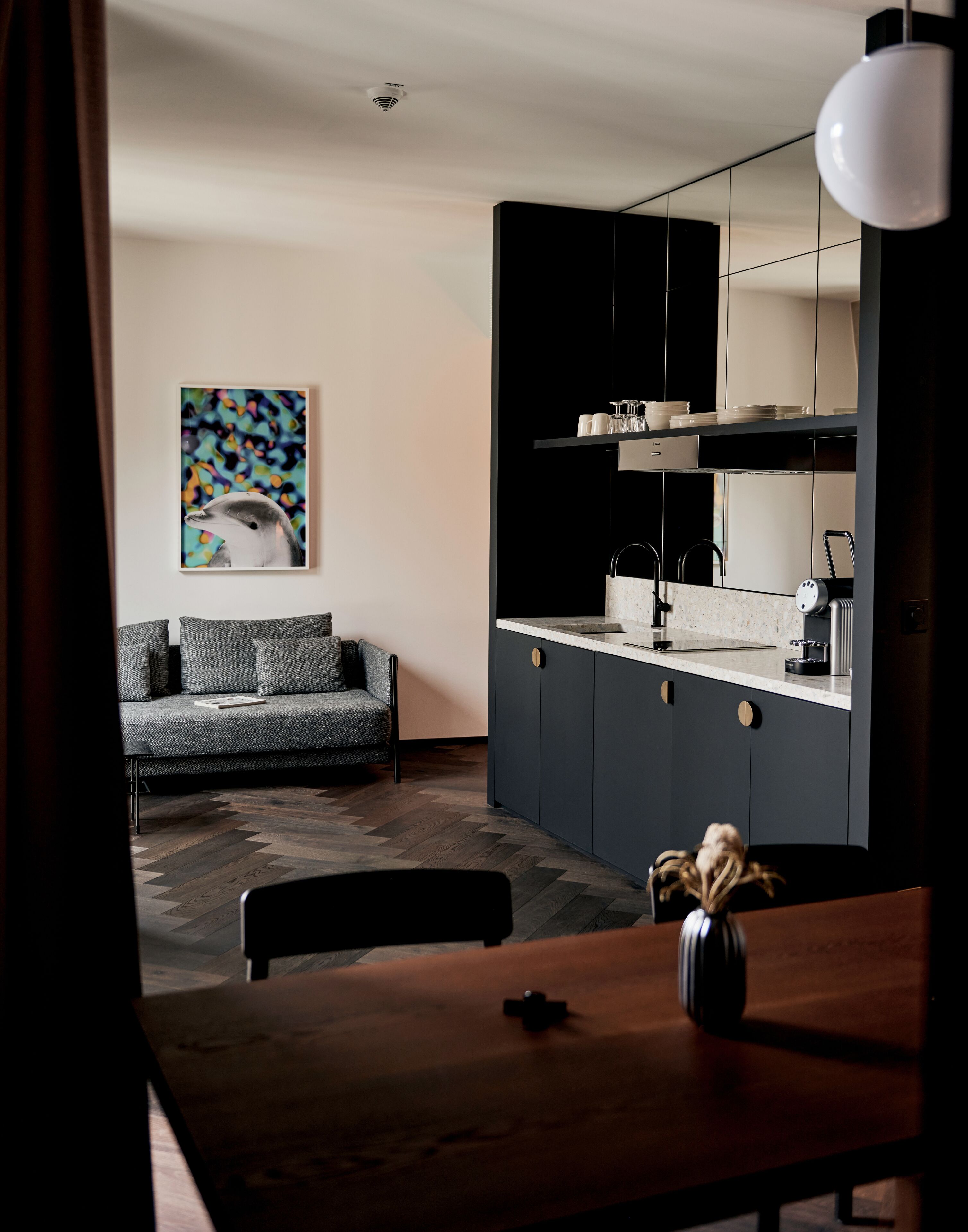 Una cucina moderna con mobili scuri, un piano di lavoro bianco e una lampada a sospensione.