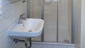 Une salle de bain moderne avec une douche à parois de verre, un lavabo blanc et un miroir doté d’étagères au-dessus.