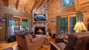A cabin interior with a stone fireplace, wooden walls, and a couch. - Cherry On Top | Cherry Log, GA (Blue Ridge)