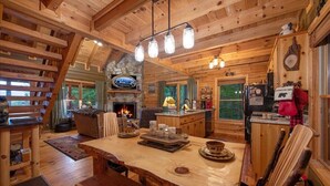 A rustic cabin interior with a stone fireplace, wooden dining table, and a cozy seating area. - Cherry On Top | Cherry Log, GA (Blue Ridge)