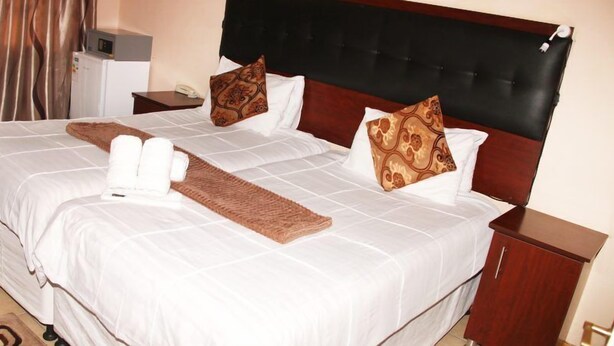 Habitación de hotel con una cama grande, dos almohadas, una mesita de noche y un mueble pequeño.