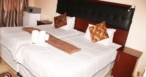 Une chambre d’hôtel avec un grand lit, deux oreillers, une table de chevet et une petite armoire.