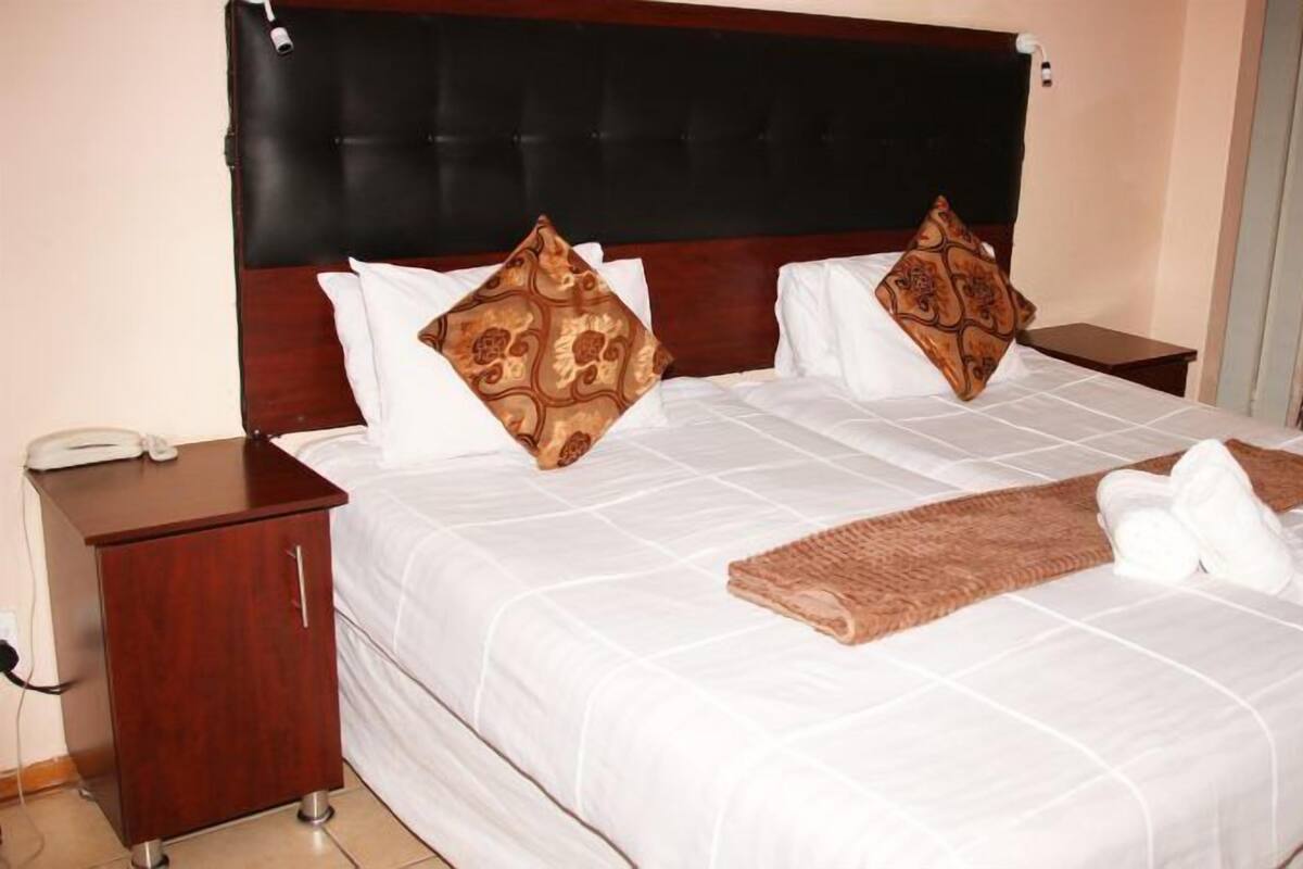 Una cama bien tendida con cabecera marrón, almohadas blancas y una manta marrón.