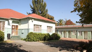 Un edificio de dos pisos con techo rojo, ventanas grandes y un estacionamiento al frente.