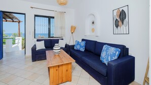 A modern living room with a blue sofa, a wooden coffee table, and a view of the sea through an open door. - Eco Beachfront Villa (Gennadi)