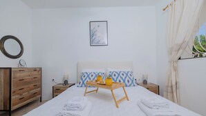 A neatly arranged bedroom with a bed, bedside tables, a wooden dresser, and a framed picture on the wall. - Eco Beachfront Villa (Gennadi)