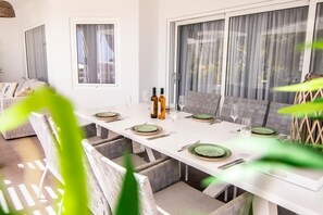Een eethoek met een witte tafel gedekt voor vier personen, groene borden en flessen wijn.