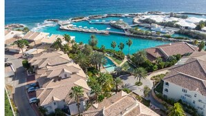 Vista aerea di un resort costiero con diverse piscine, un porto turistico ed edifici residenziali con tetti in tegole.
