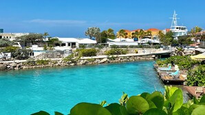 Una località balneare con una piscina turchese cristallina, un pontile con lettini e un grande yacht sullo sfondo.