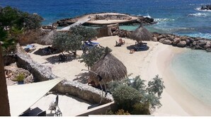 Una spiaggia con ombrelloni di paglia, sdraio e un litorale roccioso.