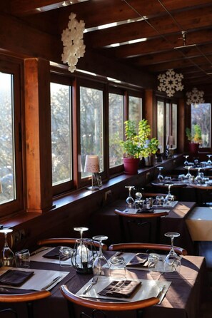 Enjoy meals in a warm and inviting dining area with tables facing expansive windows offering views of the outdoors.
