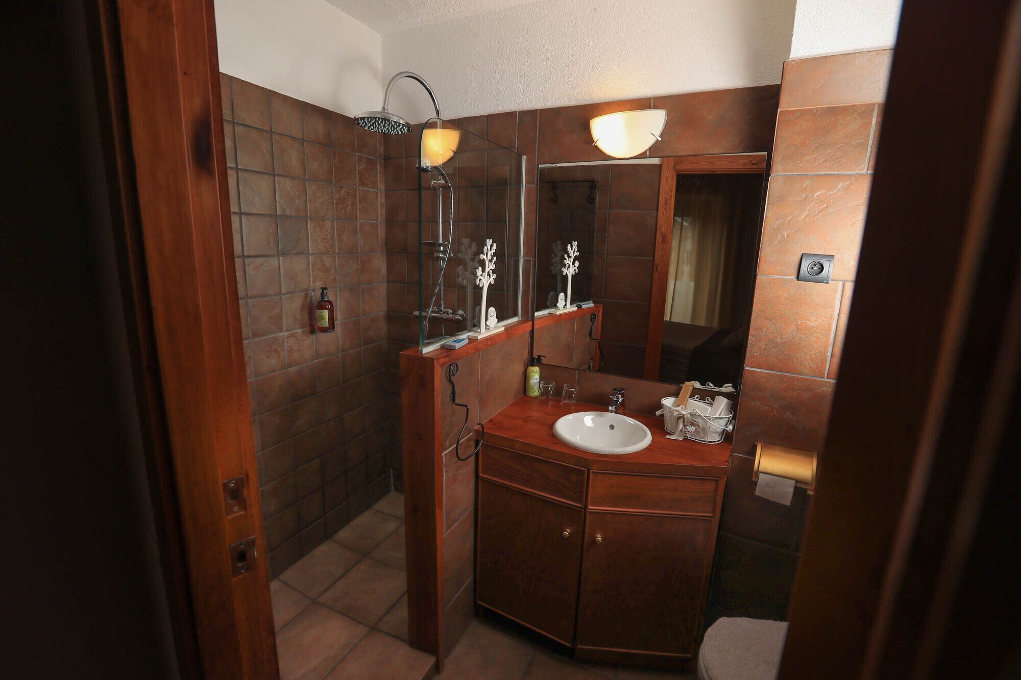 Un baño con tocador de madera, lavamanos blanco, espejo y ducha con puerta de vidrio.