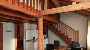 Amplia sala de estar con un alto techo de madera, una cocina al fondo y una escalera que conduce a un nivel superior.