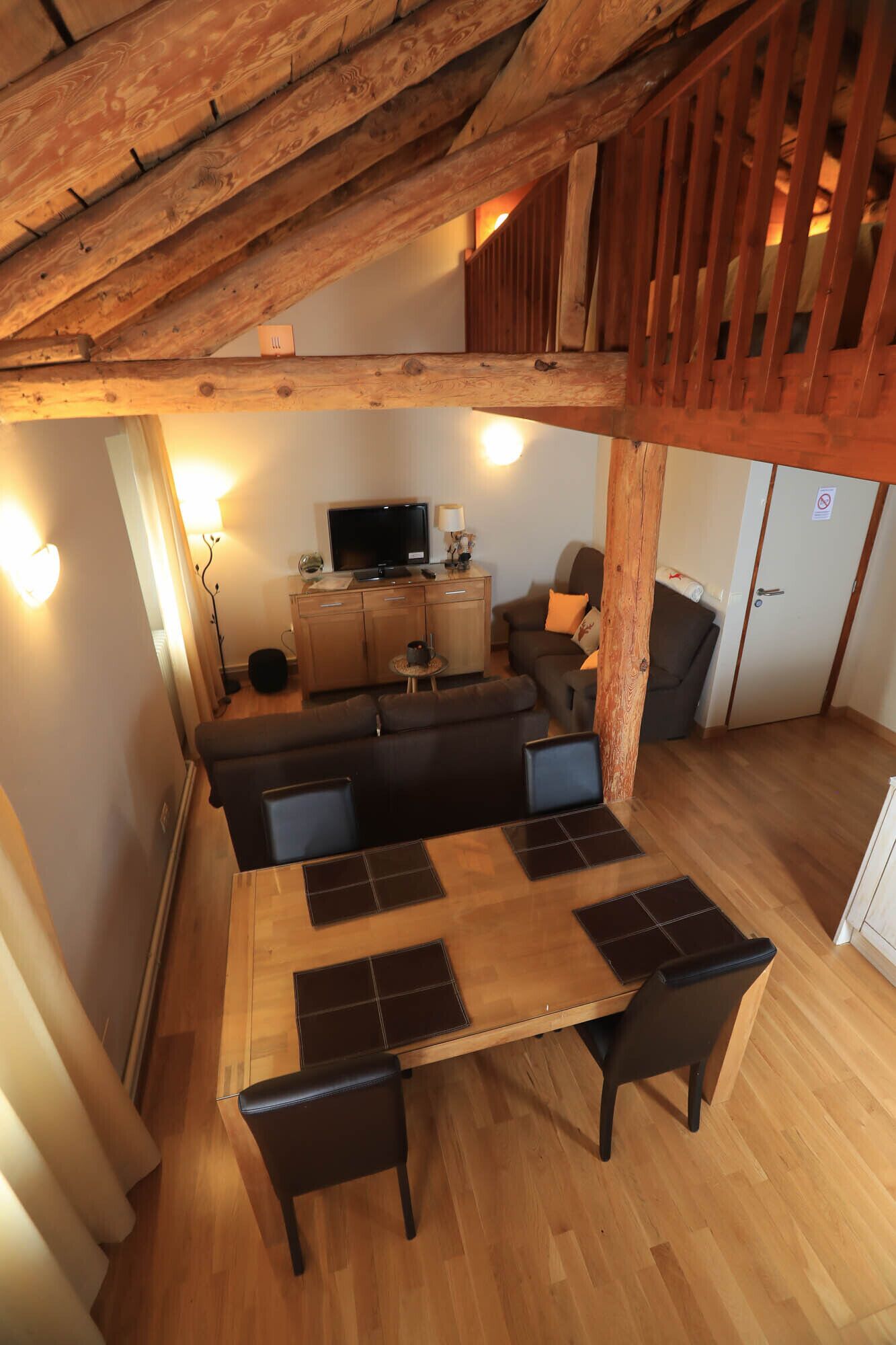 Een houten eettafel met stoelen, een bank en een televisie in een gezellige kamer met houten balken.