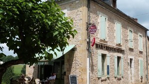 Un edificio in pietra con un'insegna per un ristorante. Tavoli e sedie all'aperto sotto un albero.