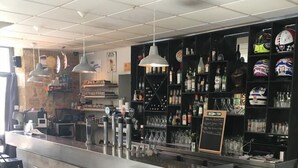 Angolo bar con un bancone, sgabelli ed scaffali con bottiglie ed elmetti.