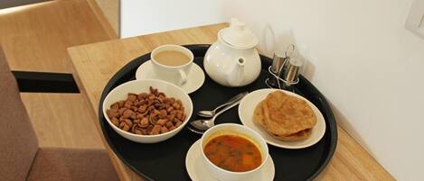 A tray with a teapot, cups, bowls of food, and a spoon on a wooden table.