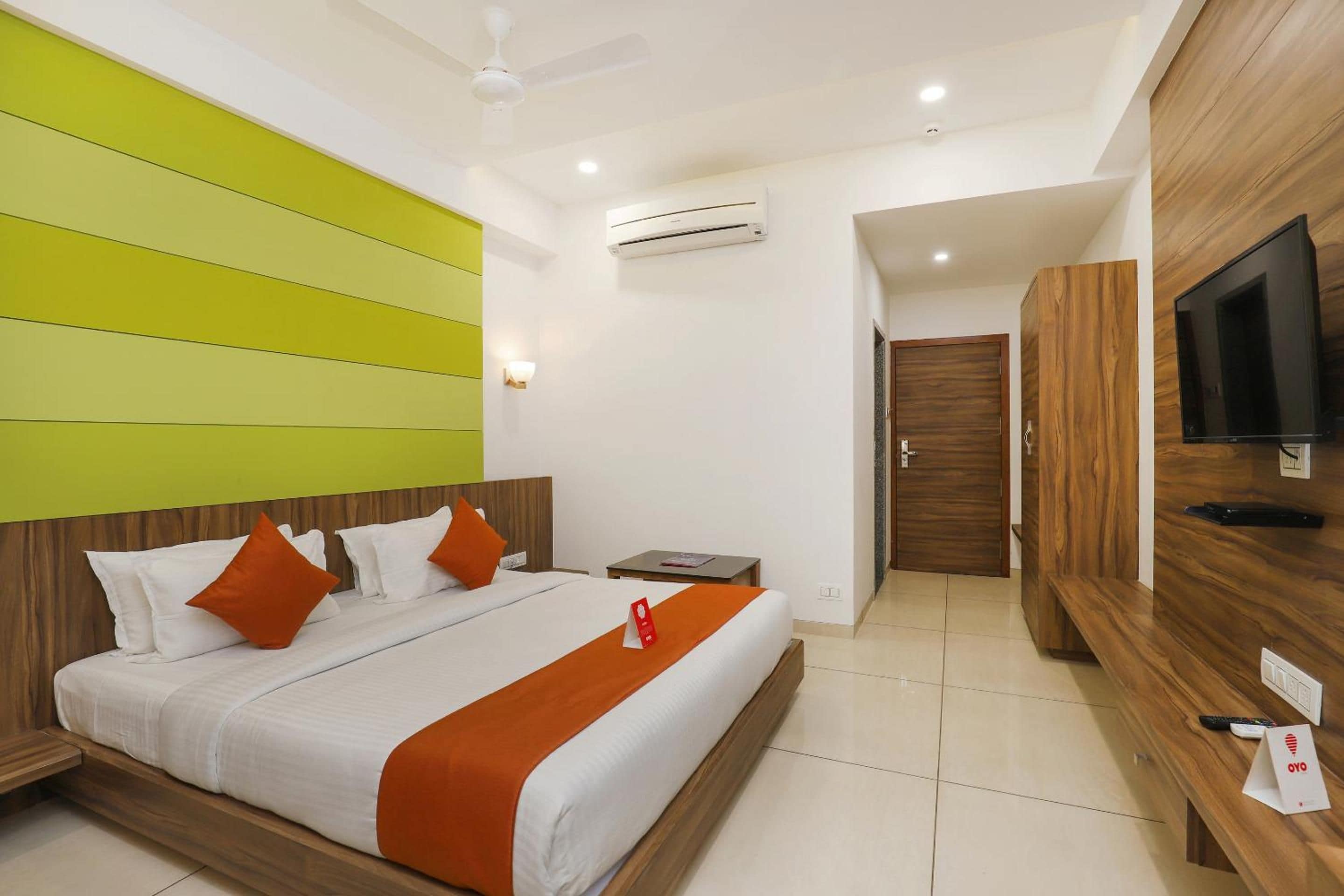 A hotel room with a bed, a television, a desk, and an air conditioning unit.