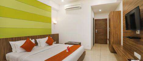 A hotel room with a bed, a television, a desk, and an air conditioning unit.
