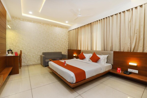 A hotel room with a large bed, a desk, a chair, and a sofa.