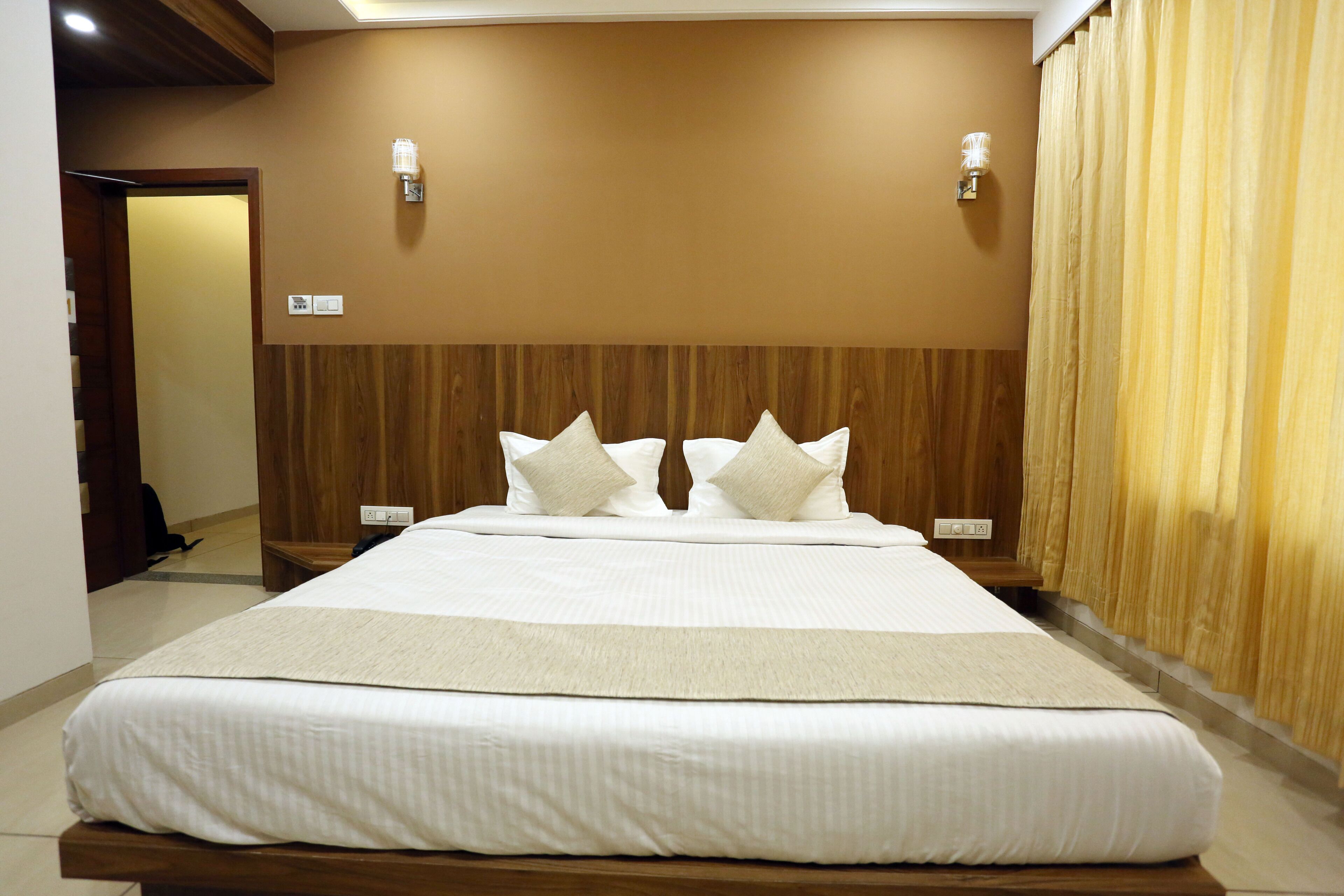 Habitación de hotel con una cama grande, cabecero de madera, dos lámparas fijadas a la pared y una cortina a la derecha.