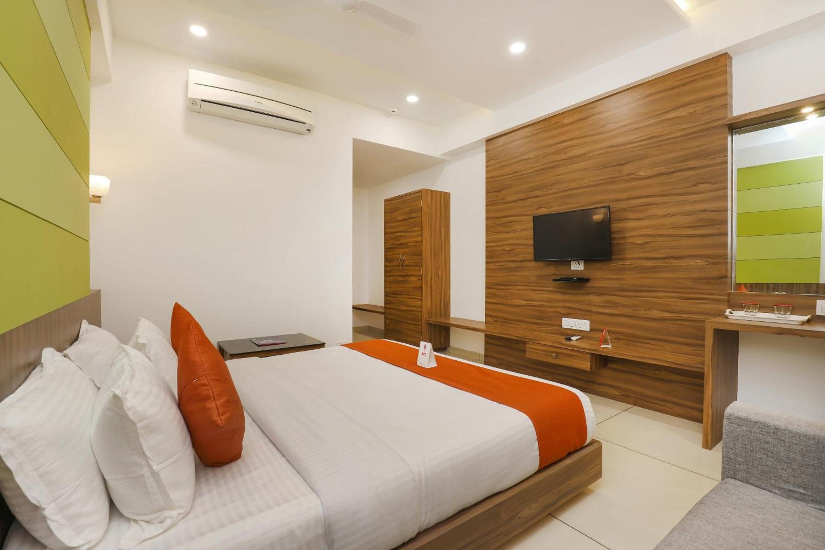 A hotel room with a bed, a TV mounted on a wooden wall, and a small desk with a chair.