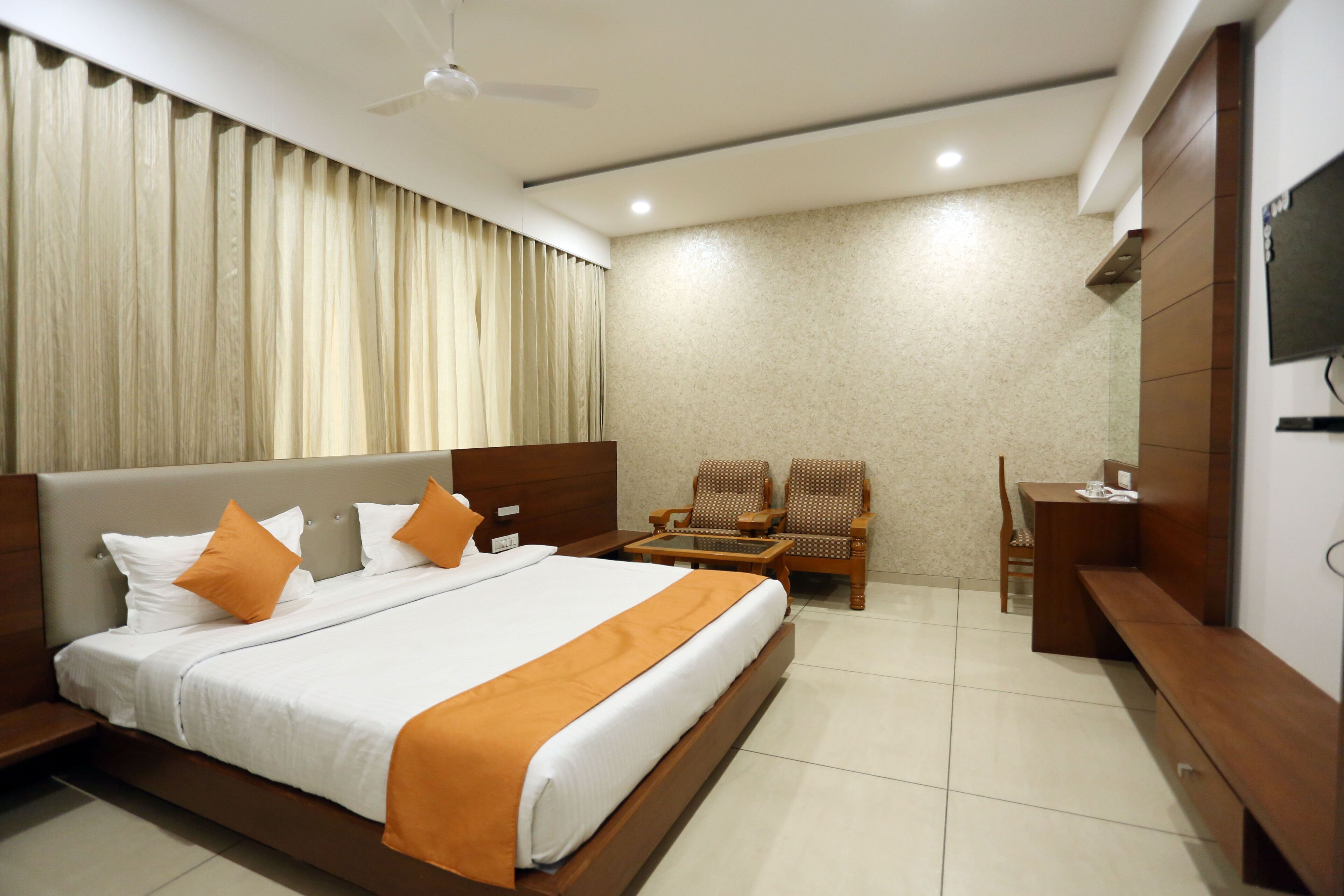 A hotel room with a large bed, a desk, two chairs, a television, and a ceiling fan.